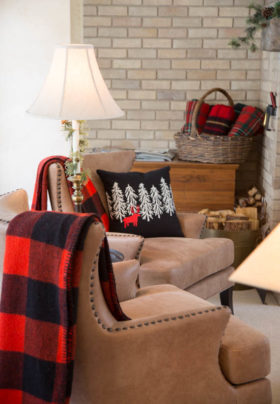 Cozy sitting room with two tan leather chairs draped by red flannel blankets and a black pillow with wintery scene