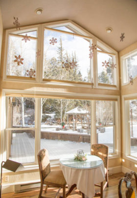 Two-story vaulted room with walls of windows, small dining room tables and chairs with beautiful winter views.