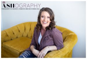 photographer Ashlee Bratton laughing while sitting on a yellow couch