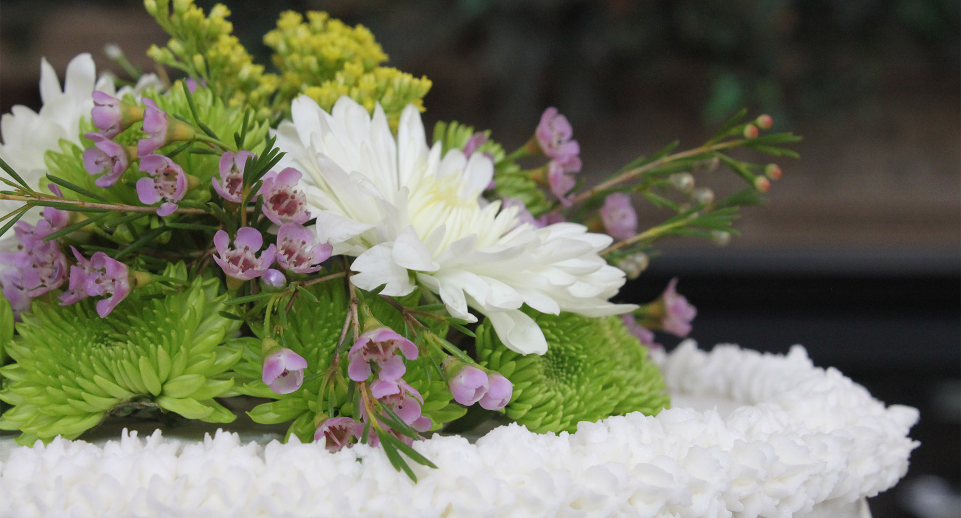 White wedding cake with topper of bright green, purple, yellow, and white flowers