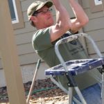 A man in a green shirt and tan hat is helping build a greenhouse