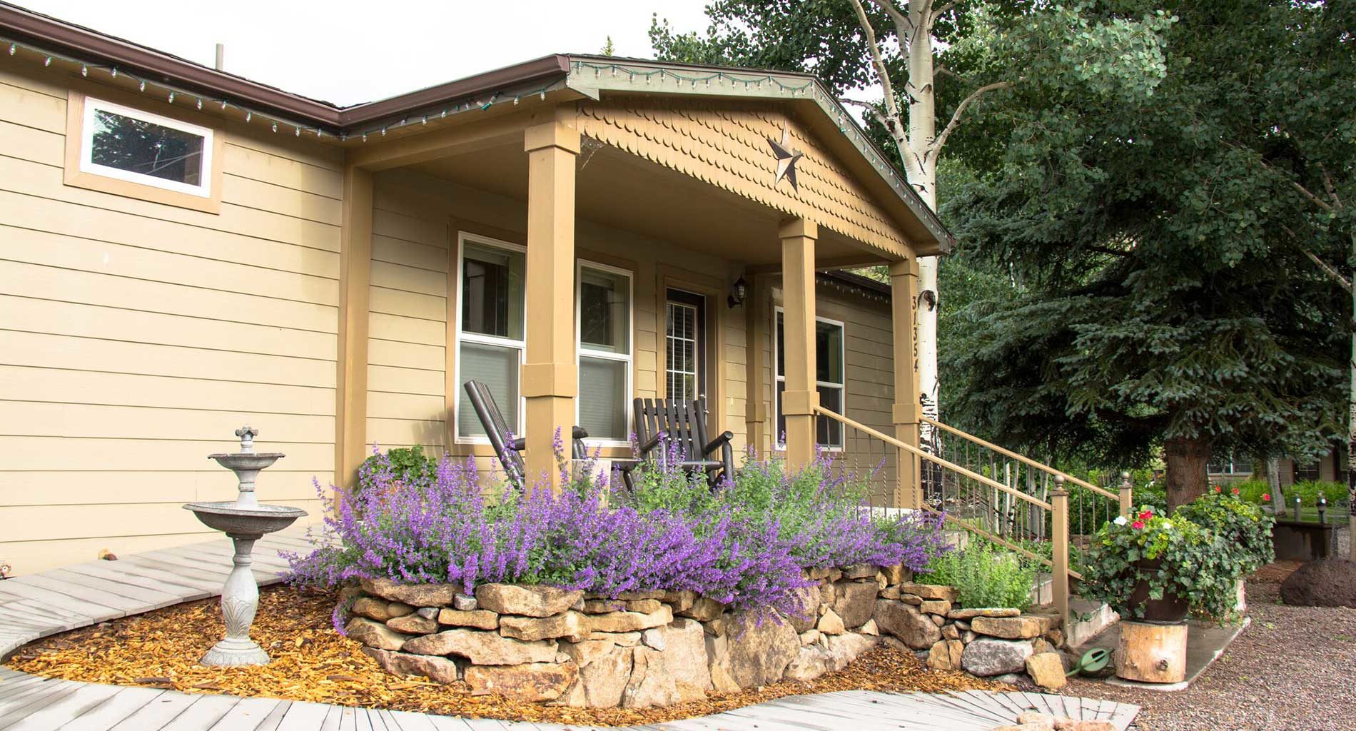 Exterior view of cabin featuring rock wall garden and lavender purples and luscious trees in background.