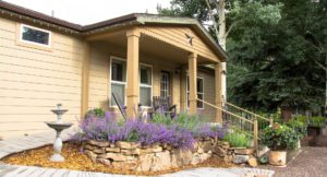 Exterior view of cabin featuring rock wall garden and lavender purples and luscious trees in background.