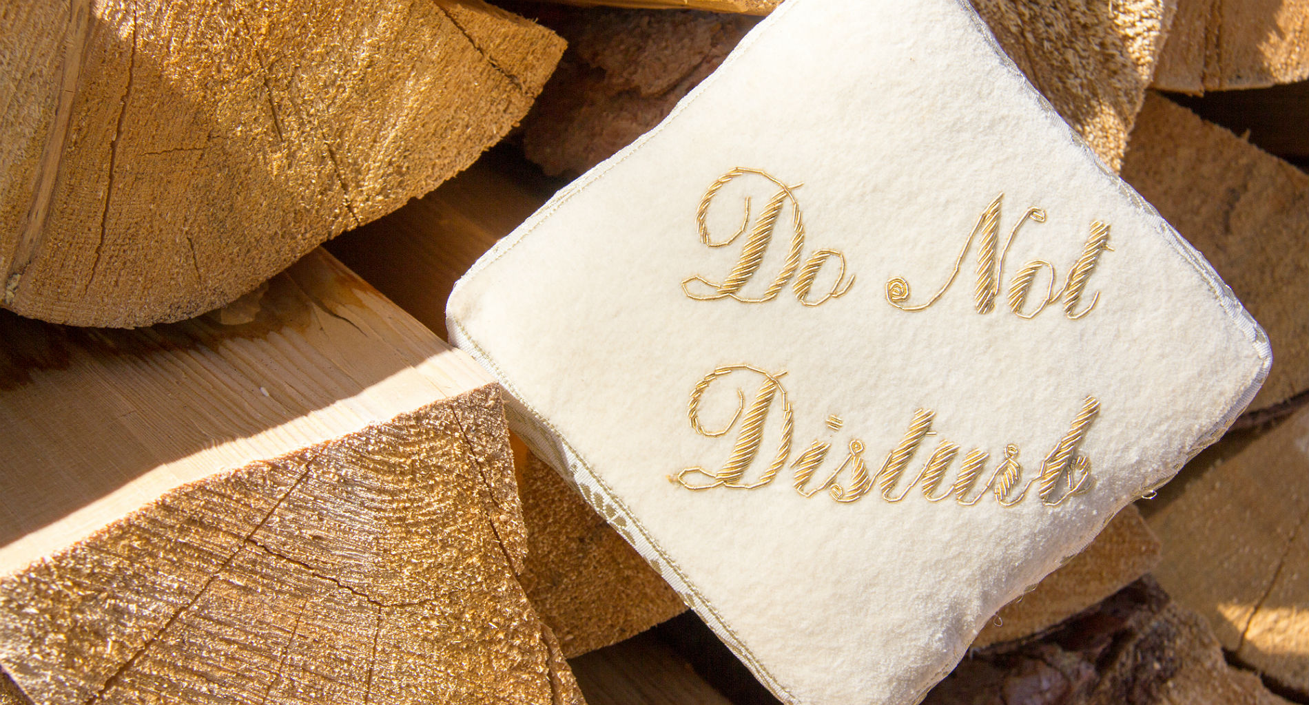 A small white pillow with gold lettering reading "Do Not DIsturb" sits among a pile of freshly cut wood