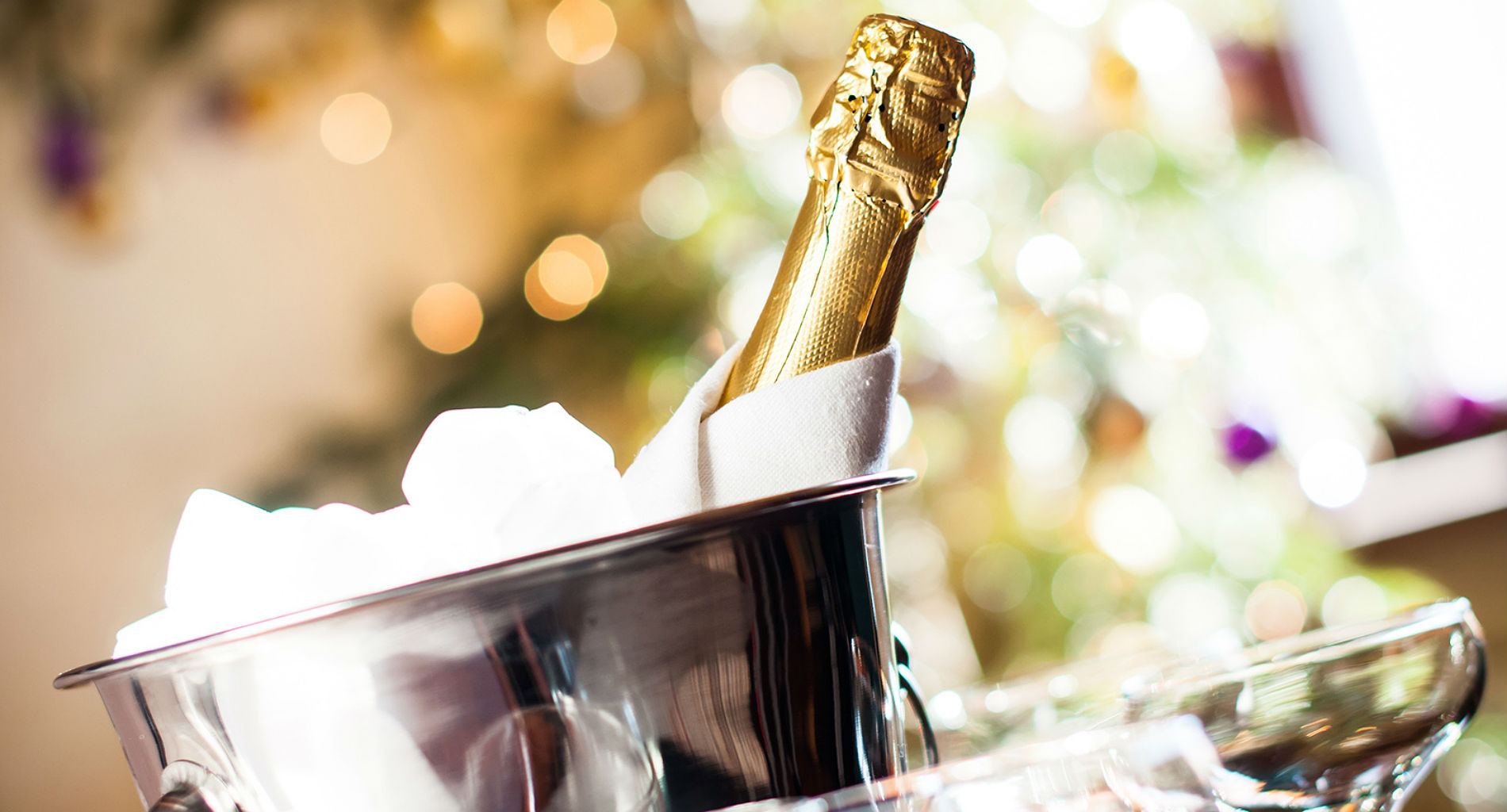 An unopened bottle of champagne wrapped in a white cloth rests in a shiny silver bucket